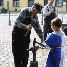Ein Kind schmiedet mit Hilfe eines Museumsmitarbeiters an der Feldschmiede
